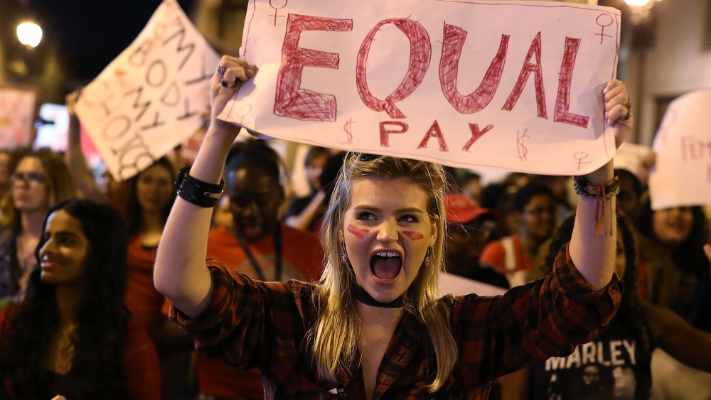Image: A protester holds a sign that readings "Equal Pay"