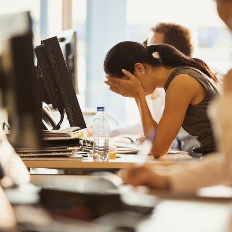 Image: Stressed woman sits with her head in her hands at an office desk