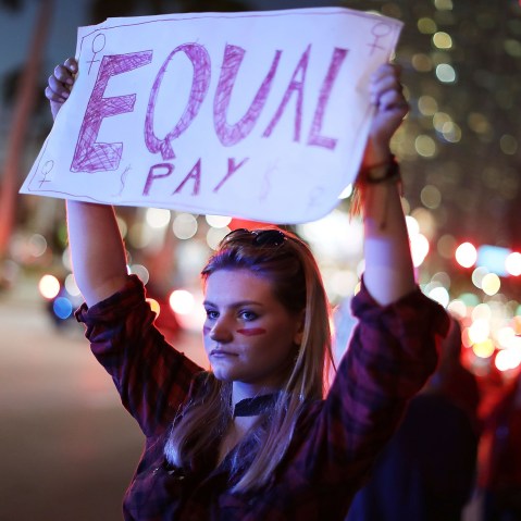 Image: A woman holds a sign that reads, "Equal Pay" during "A Day Without A Woman" demonstration in Miami