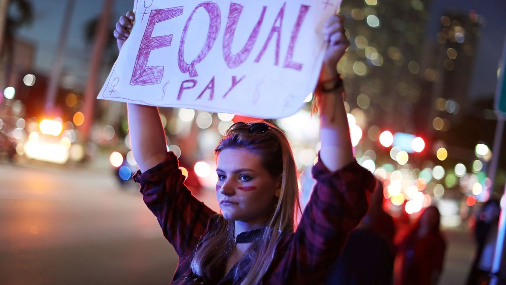 Image: A woman holds a sign that reads, "Equal Pay" during "A Day Without A Woman" demonstration in Miami