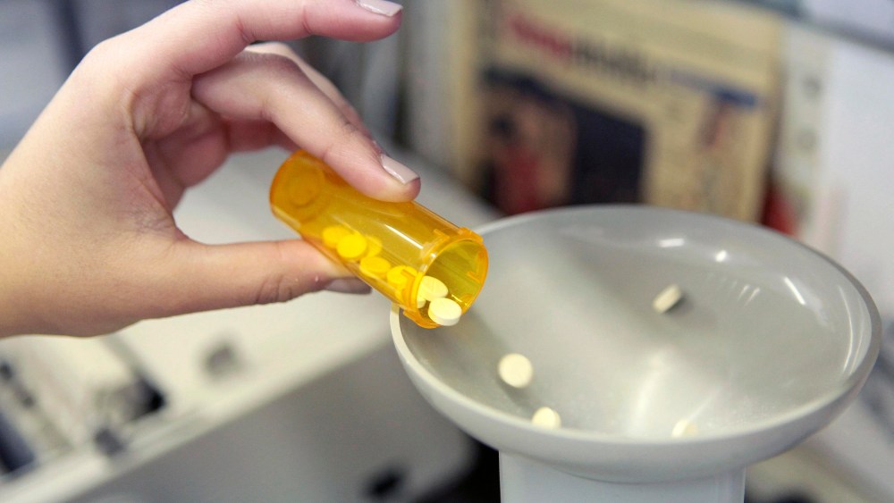 Image: A pharmacy employee dumps pills into a pill counting machine as she fills a prescription.