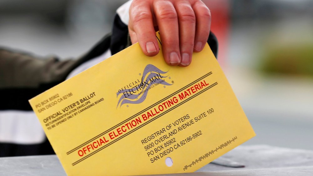 Image: A poll worker places a mail in ballot into a voting box as voters drop off their ballot in the U.S. presidential primary election in San Diego, California