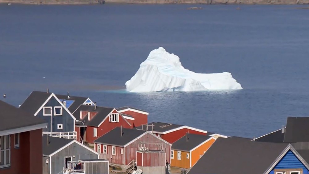 An iceberg floats past a village in Greenland.