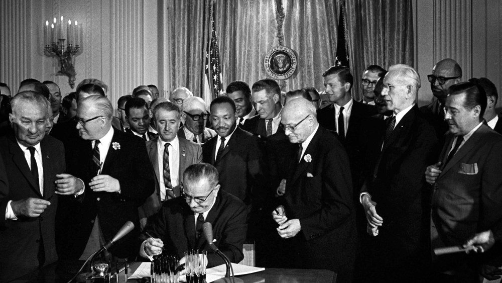 Image: President Lyndon B. Johnson signs the Civil Rights Act as Martin Luther King Jr. looks on at the White House in 1964.