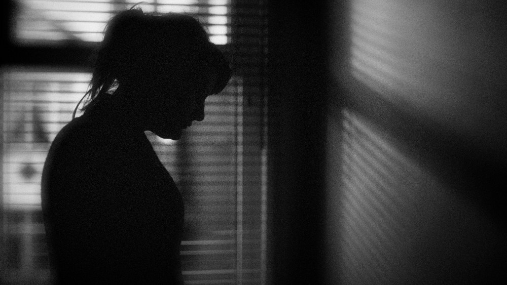 Image: The silhouette of a woman standing by a window.