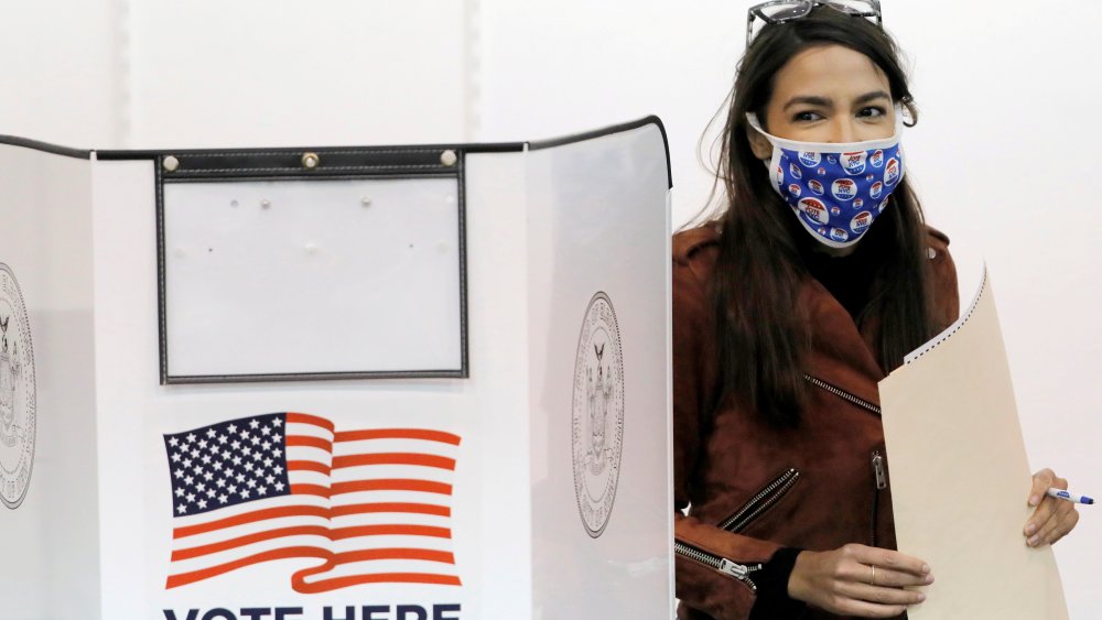 Image: Alexandria Ocasio-Cortez stands next to her voting booth holding her filled ballot.