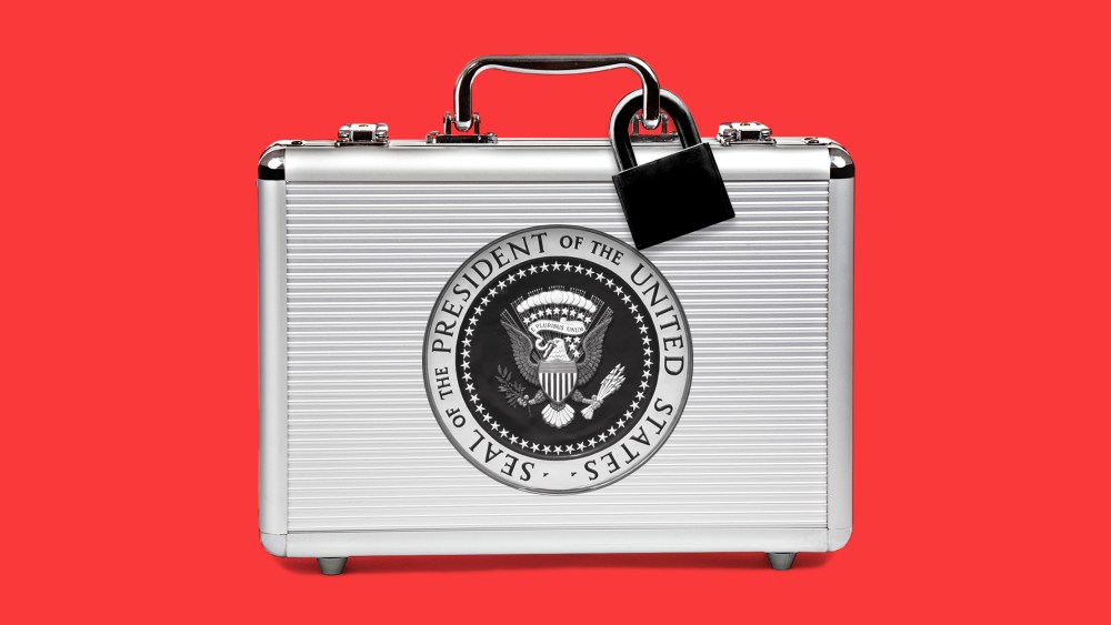 Image: A silver suitcase with a black lock and the seal of the President of the United States sits against a red background