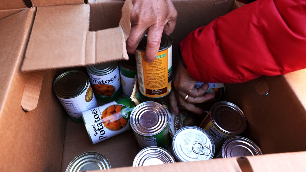 Image: Hands sort through cans of sweet potatoes in a cardboard box