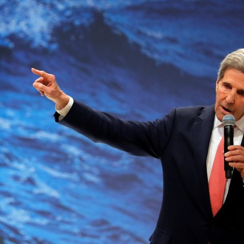Image: John Kerry holding a mic against a background of waves