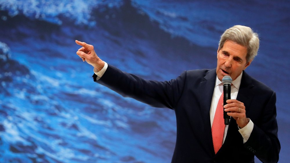 Image: John Kerry holding a mic against a background of waves