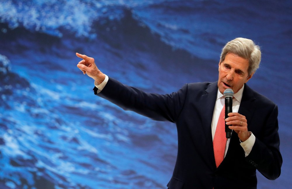 Image: John Kerry holding a mic against a background of waves