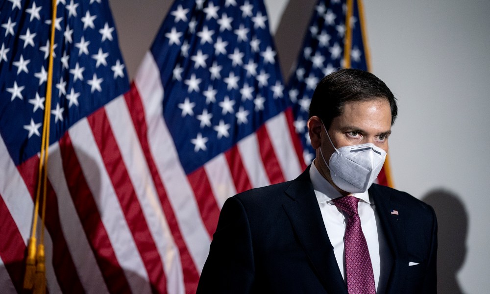 Image: Marco Rubio in a mask stands against U.S. flags