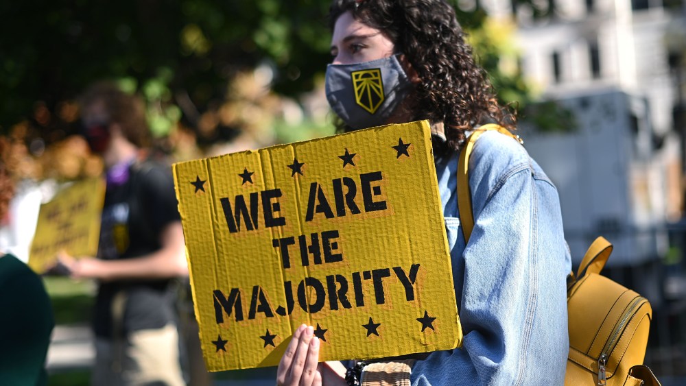 Image: A girl holds a yellow placard that reads,"We are the majority".
