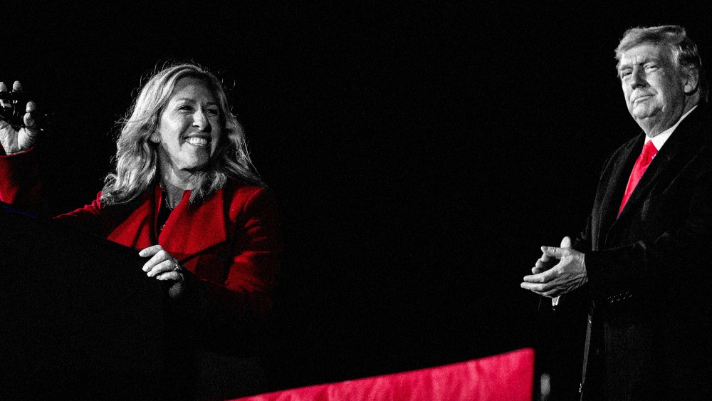Image: Marjorie Taylor Greene speaks on stage and Donald Trump applauds in the background.