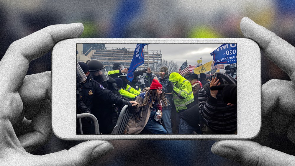 Photo illustration of a hands holding a phone with the image of Trump supporters clashing with the police and security forces as people try to storm the US Capitol.