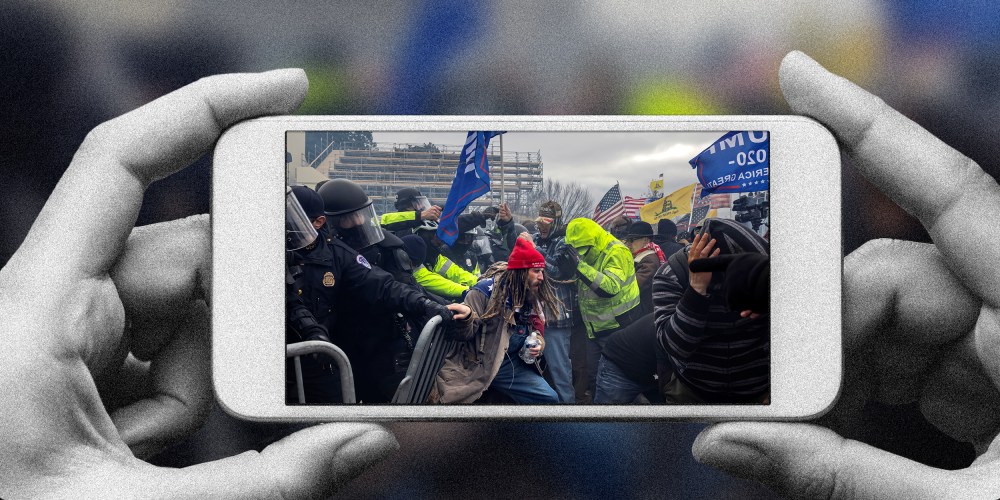 Photo illustration of a hands holding a phone with the image of Trump supporters clashing with the police and security forces as people try to storm the US Capitol.