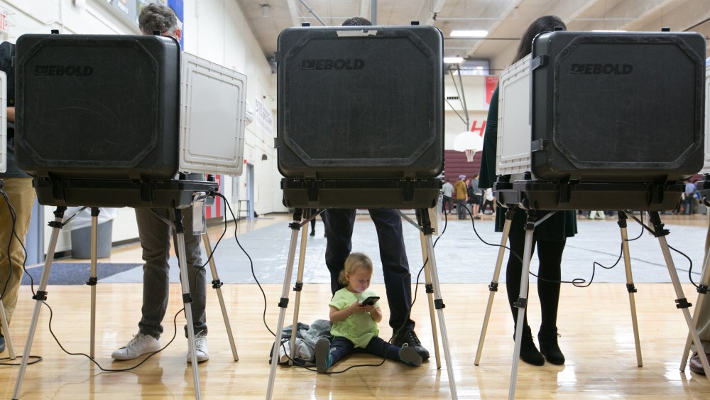 Image: A child waits between her father's legs as he and other voters cast their ballots for the mid-term elections