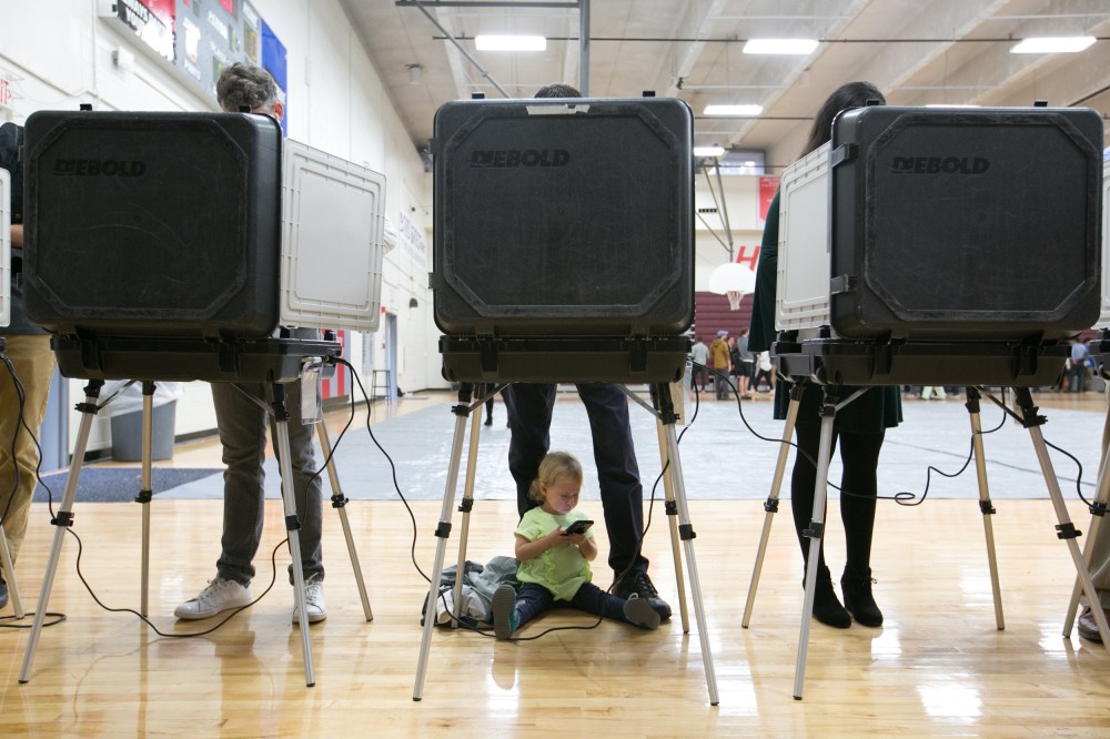 Image: A child waits between her father's legs as he and other voters cast their ballots for the mid-term elections