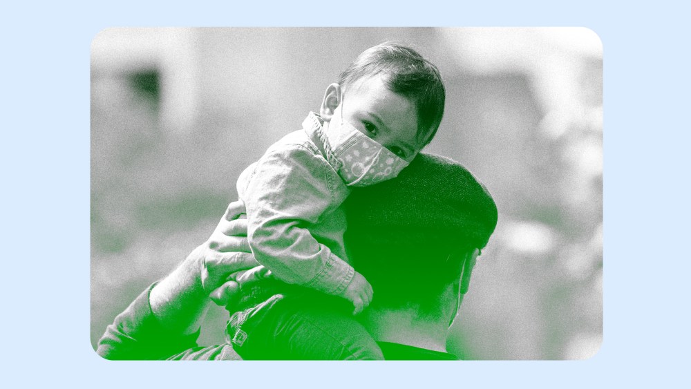 Image: A young child wearing a mask sits on his fathers shoulders.