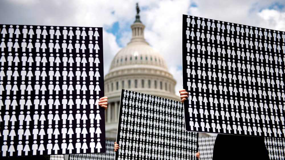 Image: Hands holding up placards representing people against the Capitol Hill in the background.