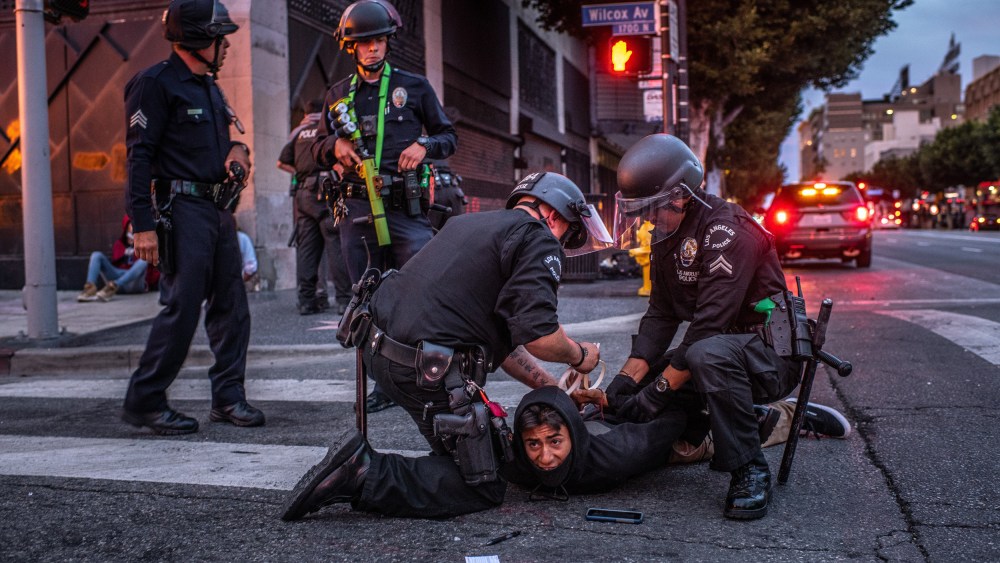 Image: Two police officers detain and handcuff a person on the street and two police officers stand by.