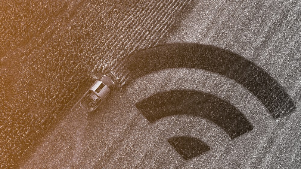 Photo illustration of harvester gathering corn crop in a field and the cultivated part of the land is in the shape of the wireless connectivity symbol.