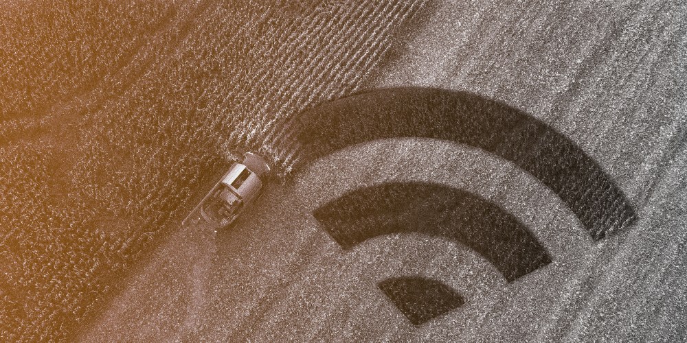 Photo illustration of harvester gathering corn crop in a field and the cultivated part of the land is in the shape of the wireless connectivity symbol.