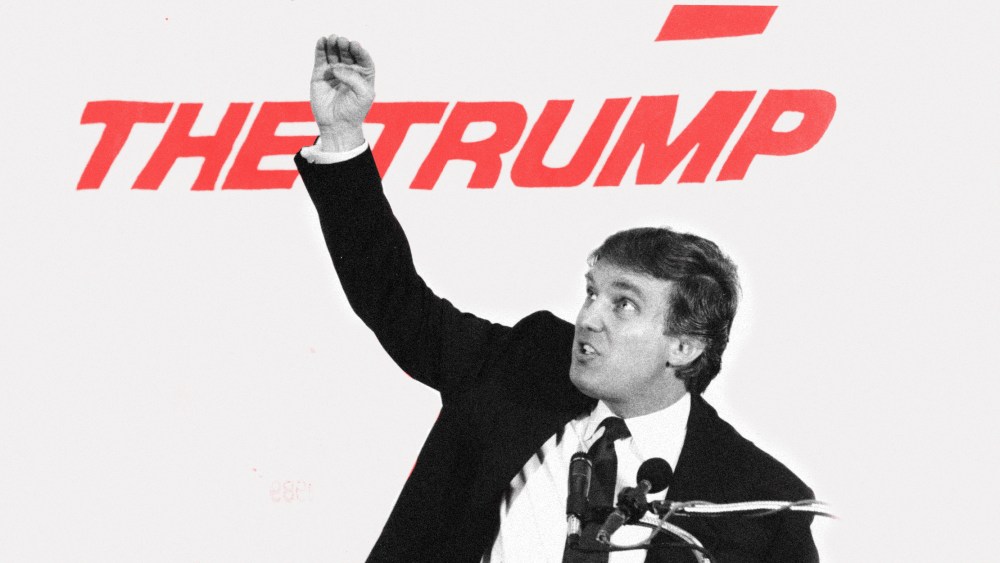 Image: Young Donald Trump speaking at a podium. Text behind him partially reads, "The Trump"