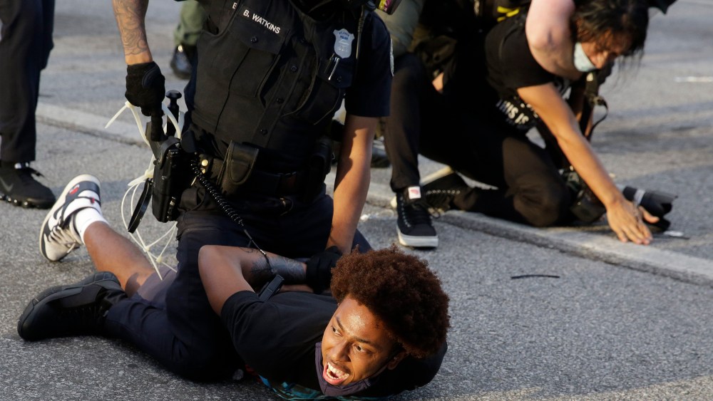 Image: Protestors being detained by police officers.