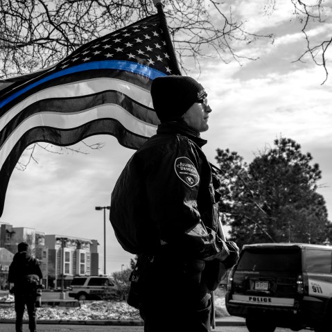 Image: A police officer with a Blue Lives Matter flag in a procession route during a memorial service.