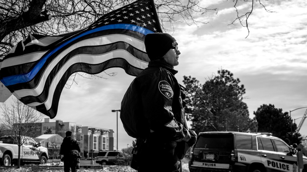 Image: A police officer with a Blue Lives Matter flag in a procession route during a memorial service.
