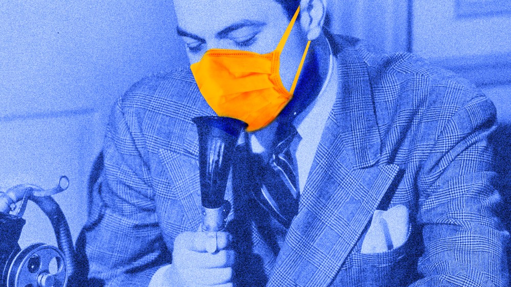 Photo illustration: A person wearing a suit and a protective mask speaking into a dictaphone.