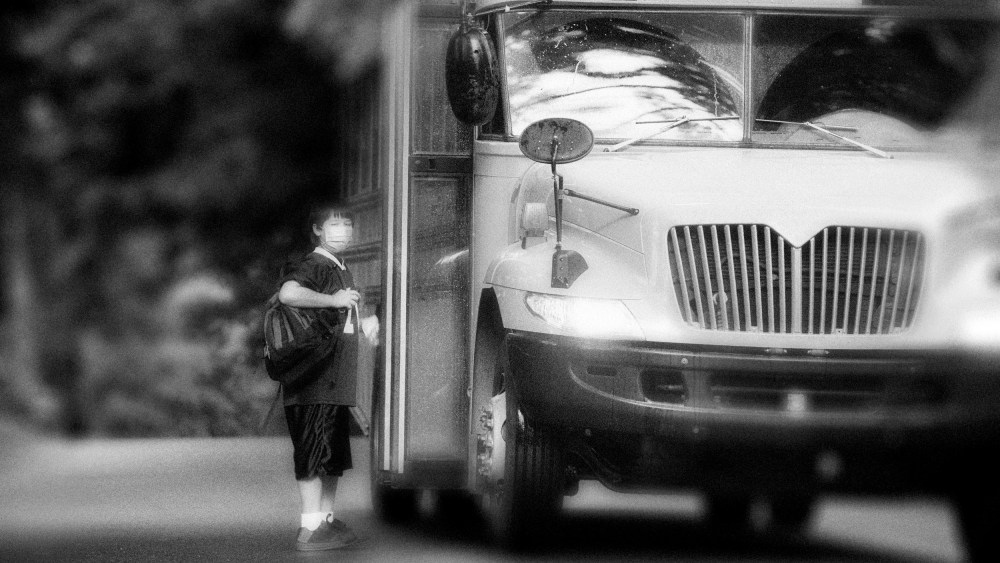 Image: School bus picking up elementary student wearing surgical mask.