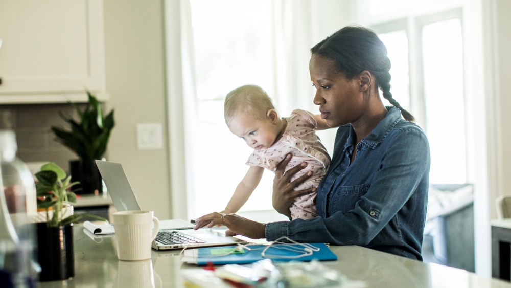 Mother holding baby while using laptop/working from home