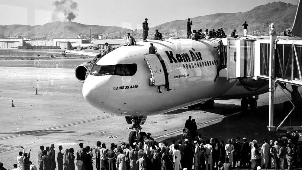 Image: Afghan people climb atop a plane as they wait at the Kabul airport.