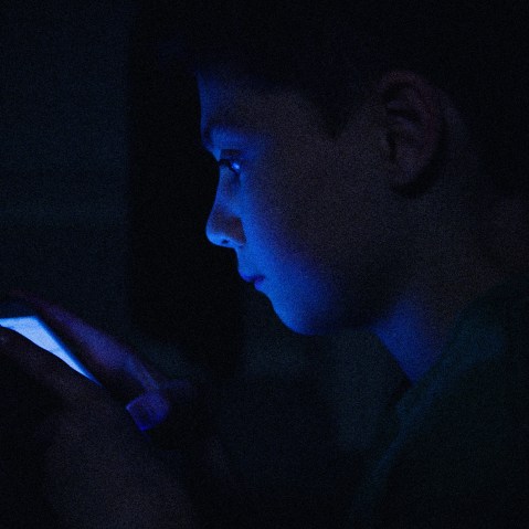 IMage: a teenage boy on his phone, face illuminated in the dark