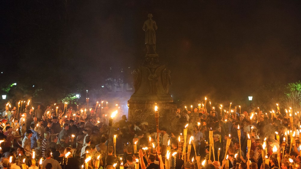 Image: People gather around the base of a statue with torches.