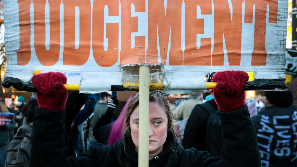 Image: A woman holding up a sign that reads,"Judgement".