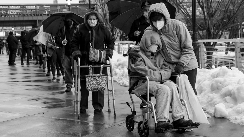 Image: A person in a wheelchair in a line of people lined up outside a Covid-19 vaccination site.