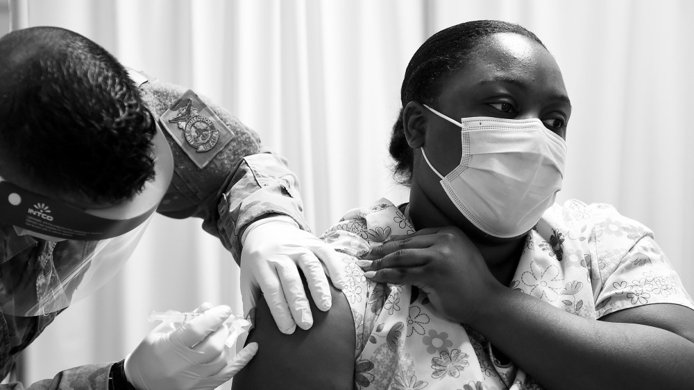 Image: A person wearing scrubs receiving a vaccine.
