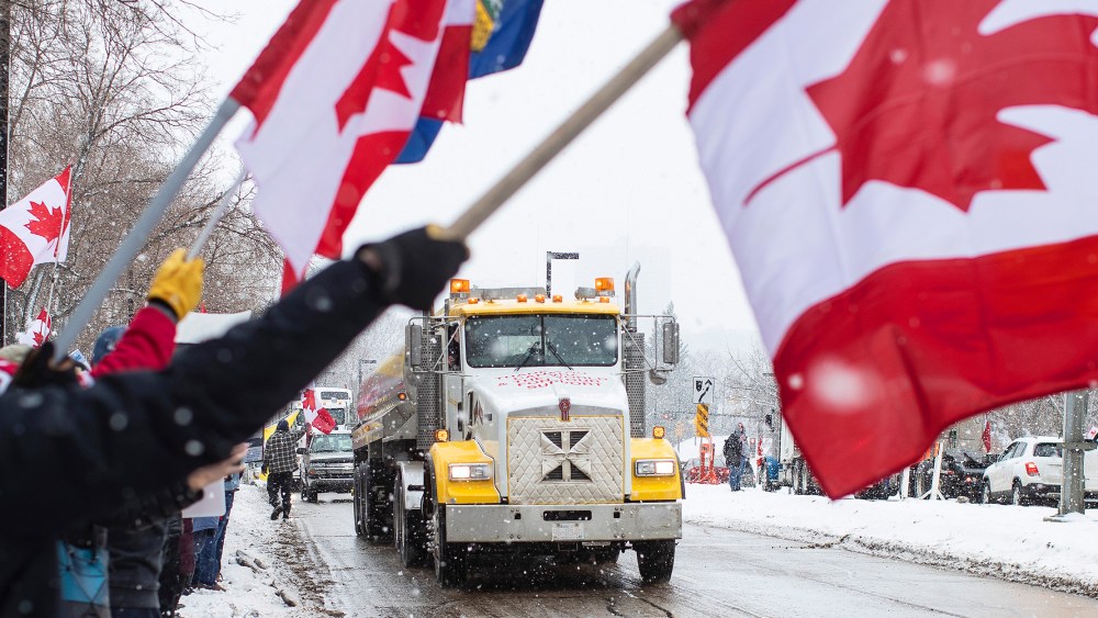 Image: People waving the Canadian flag in protest as a truck passes by.