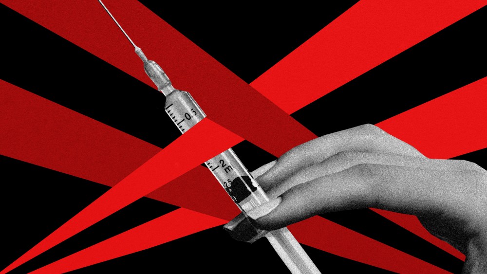 Photo illustration: A hand holding a vaccine syringe blocked by red spotlights from either sides.