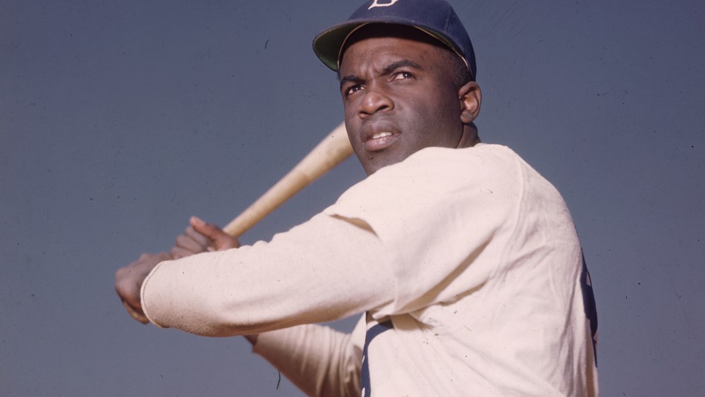 Image: A portrait of the Brooklyn Dodgers' Jackie Robinson in uniform, preparing to swing a baseball bat.