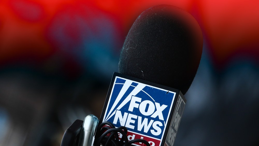 Photo illustration: Red color overlay over an image of a microphone with the Fox News logo.