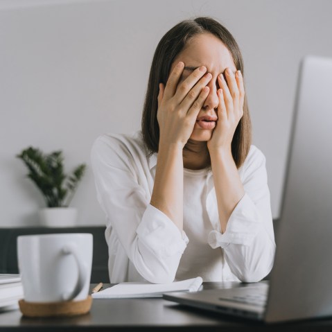 A woman sitting at desk holds her head in her hands.
