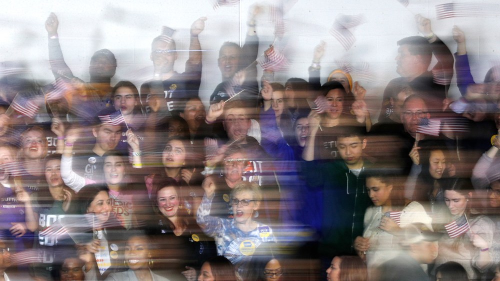 Image: Blurry image of supporters waving flags at democratic presidential candidate Pete Buttigieg's caucus night watch party in Iowa.