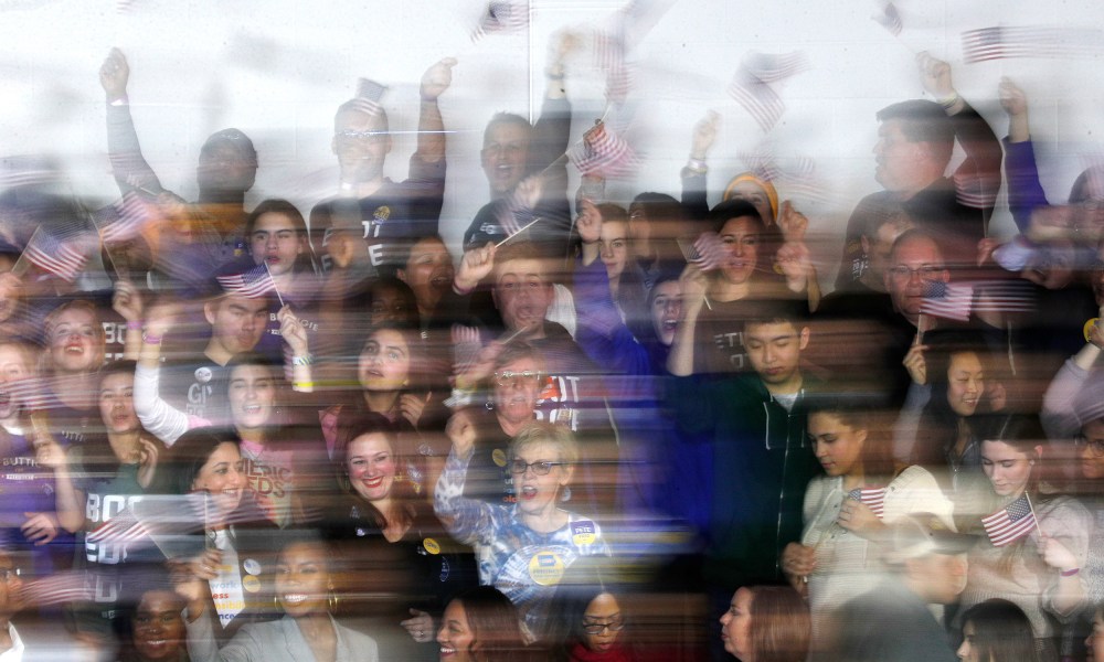Image: Blurry image of supporters waving flags at democratic presidential candidate Pete Buttigieg's caucus night watch party in Iowa.