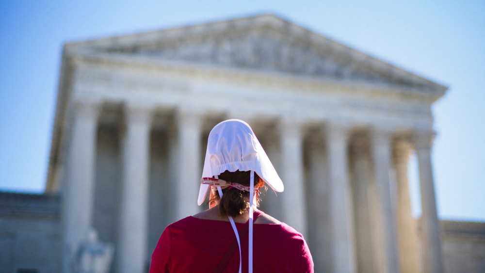 Image: Back of a pro-choice demonstrator wearing a red gown and a white hat outside the U.S. Supreme Court.