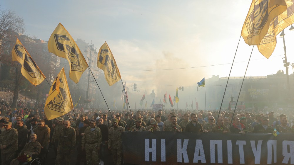 Image: People in the uniform carrying Azov battalion flags and a banner saying "No Capitulation" through the smoke during a rally in Kyiv, Ukraine, Oct. 14, 2019.