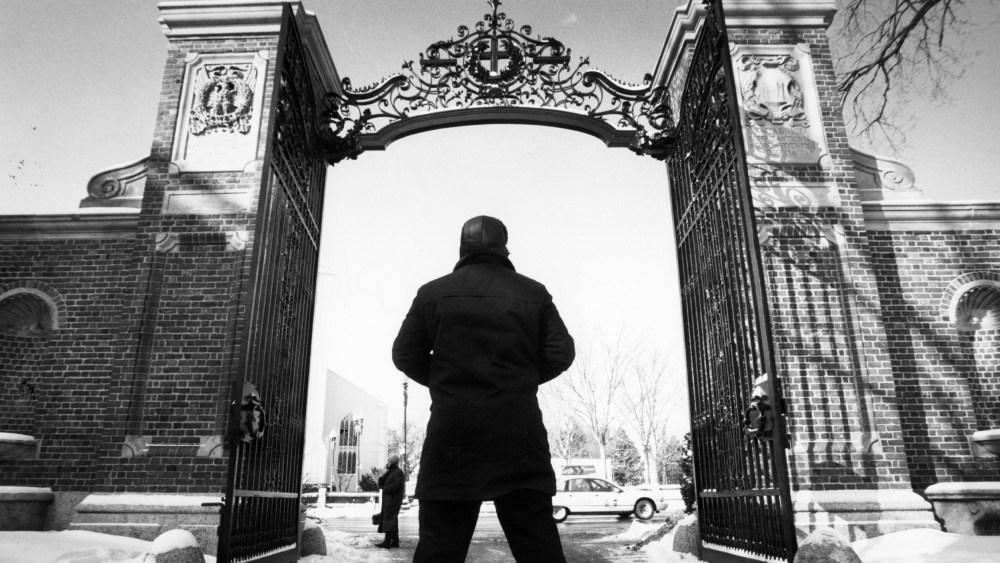 Image: A guard looking up at the gate to Harvard Yard at Harvard University.